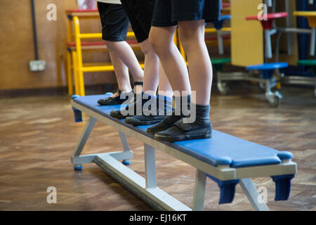 Three UK school children standing on a bench in a PE lesson in a school hall Stock Photo
