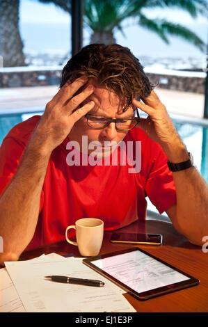 Mature man in holiday setting concentrating on financial statements and business papers along with his iPad Air tablet computer Stock Photo