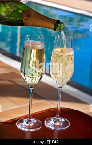 Close view on pouring chilled glasses of cava on sunlit terrace with luxury infinity pool in background Stock Photo