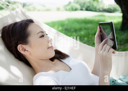 Young woman lying down on the hammock and using touch pad, Stock Photo