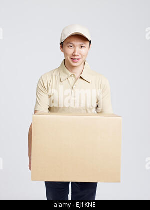 male asian delivery man carrying large cardboard box. Stock Photo