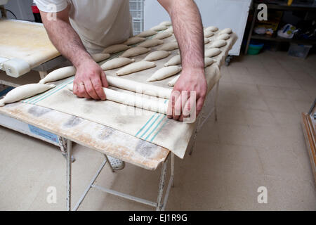 Male baker kneading and placing pieces of bread over fermentation sheet. Manufacturing process of spanish bread Stock Photo