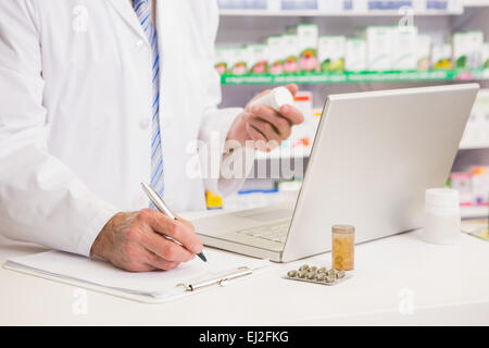 Pharmacist writing on clipboard and holding medication Stock Photo