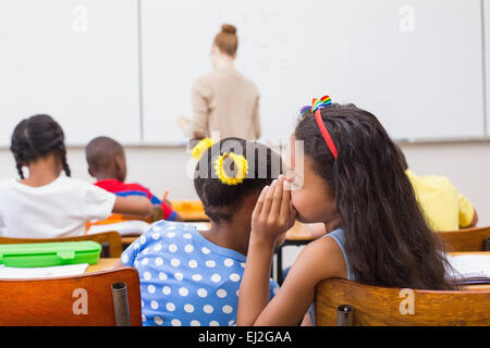 Cute pupils whispering in classroom Stock Photo