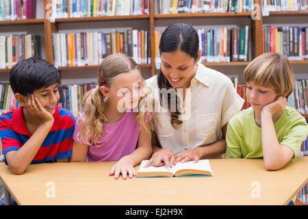Cute pupils and teacher reading in library Stock Photo