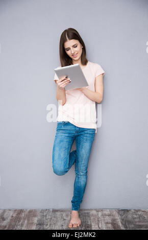 Young woman using tablet computer and leaning on the gray wall Stock Photo
