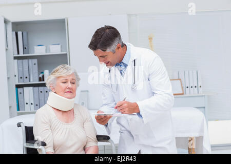Doctor writing prescription for patient wearing neck brace Stock Photo