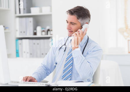 Doctor using telephone while working on computer Stock Photo