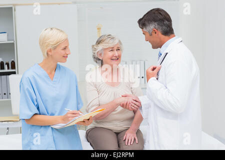 Doctor and patient shaking hands while nurse writing reports Stock Photo