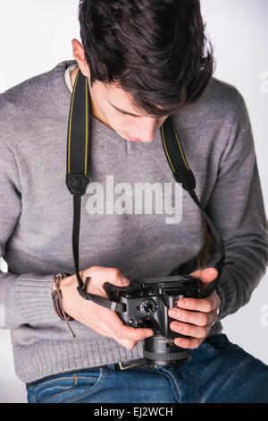 Handsome young male photographer looking at photographs on his professional photo camera's display hanging from his neck, isolat Stock Photo