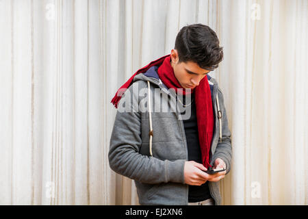 Young man standing indoor typing a text message on his phone  with his fingers as he communicates with friends Stock Photo
