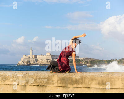 26 year Hispanic Cuban female model posing in maroon dress on the Malecón wall with historic Morro Castle in background. Stock Photo