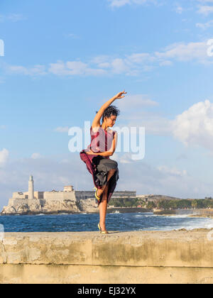 26 year Hispanic Cuban female model posing in maroon dress on the Malecón wall with historic Morro Castle in background. Stock Photo