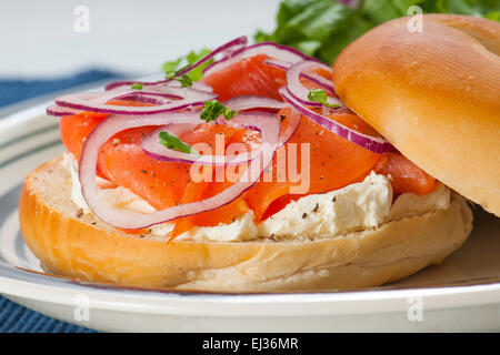 Bagel with Smoked Salmon Lox, cream cheese and red onion accompanied by lettuce salad. Stock Photo