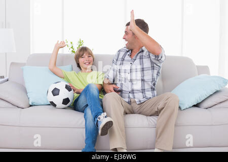 Father and son giving high-five while watching soccer match Stock Photo