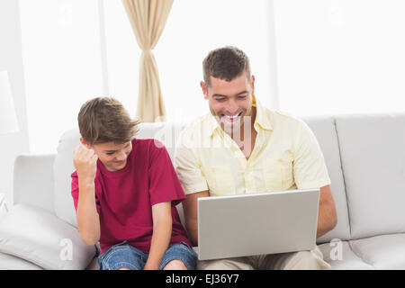 Father and son with laptop sitting on sofa Stock Photo
