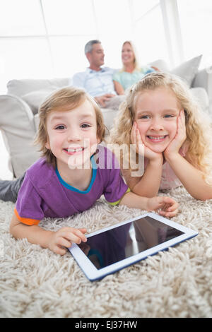 Siblings with digital tablet lying on rug Stock Photo