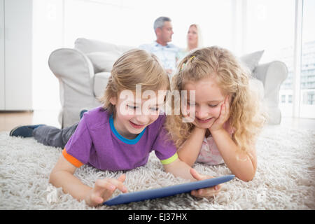 Siblings using digital tablet on rug at home Stock Photo