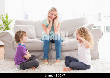 Upset mother looking at children fighting on rug Stock Photo