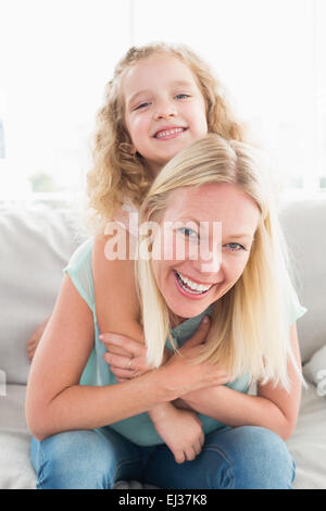 Happy mother piggybacking daughter on sofa Stock Photo