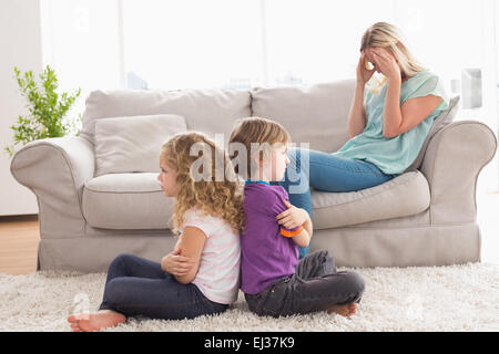 Angry siblings sitting arms crossed with upset mother on sofa Stock Photo
