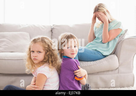 Angry siblings sitting arms crossed with sad mother on sofa Stock Photo