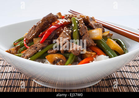 Asian flavored stir fried beef with green beans, mushrooms, peppers, carrots, and onions, with a bowl of rice and chop sticks Stock Photo