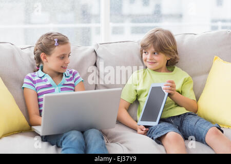 Happy siblings using technologies on sofa Stock Photo