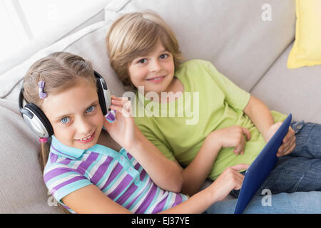 Siblings using digital tablet while listening music on sofa Stock Photo