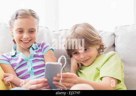 Siblings listening music through mobile phone at home Stock Photo