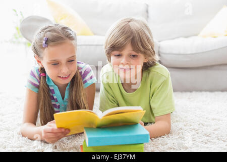Siblings reading book while lying on rug Stock Photo