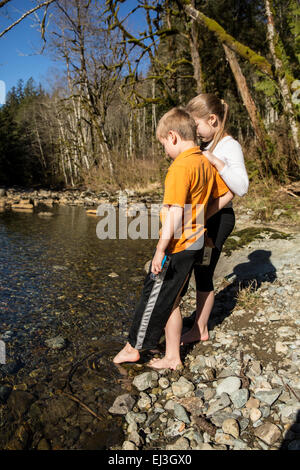 Seven year old boy and his nine year old sister gingerly testing the coldness of the  Snoqualmie River, with their toes Stock Photo