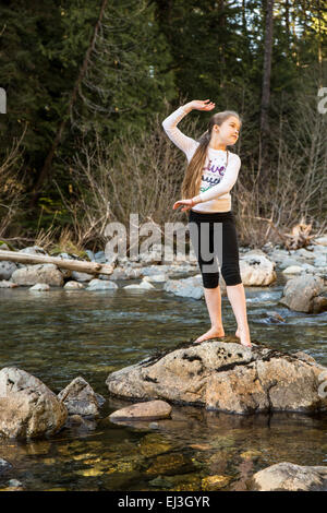 Nine year old girl lost in thought, dancing on a boulder in a shallow Snoqualmie River, near North Bend, Washington, USA Stock Photo