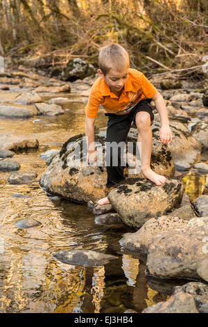 Seven year old barefoot boy climbing on rocks in the Snoqualmie River near North Bend, Washington, USA Stock Photo