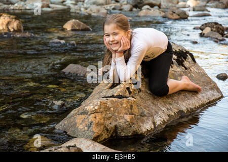 Nine year old girl playfully 'riding a rock' in the Snoqualmie River, in Olallie State Park, near North Bend, Washington, USA Stock Photo