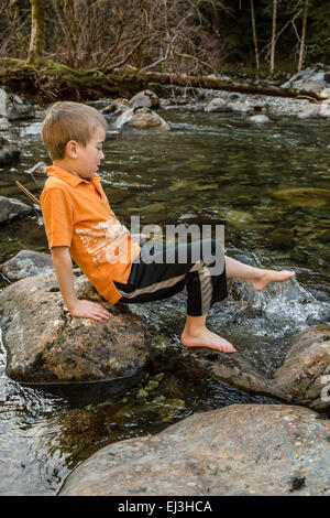 Seven year old boy splashing his foot in the cold north fork of the Snoqualmie River, near North Bend, Washington, USA Stock Photo