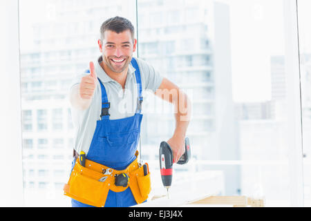 Happy handyman drilling hole in plank while gesturing thumbs up Stock Photo