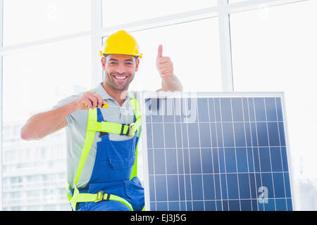 Male worker tightening solar panel while gesturing thumbs up Stock Photo