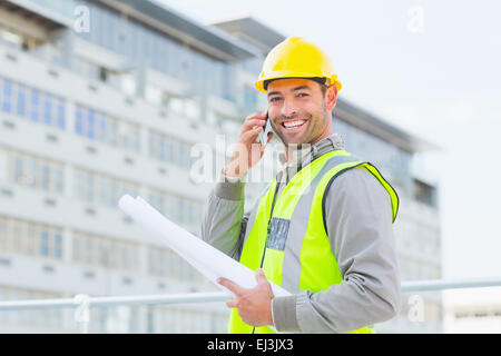 Smiling male architect with blueprints talking on mobile phone Stock Photo