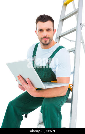 Carpenter sitting on ladder using laptop Stock Photo