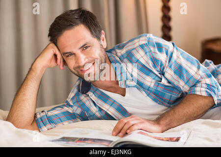 Handsome man relaxing on his bed reading magazine Stock Photo