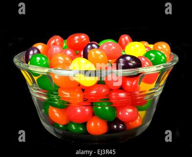 Fruit jelly beans in many colors in a glass bowl on a black background. Stock Photo