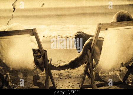 Composite image of cute couple holding hands while lying on their deck chairs Stock Photo