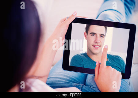 Composite image of smiling handsome man relaxing on couch using tablet Stock Photo