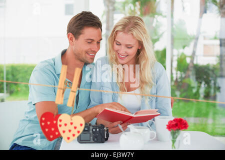 Composite image of cute hipster couple reading book together at table Stock Photo