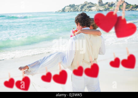 Composite image of handsome groom carrying his beautiful wife out to the water Stock Photo