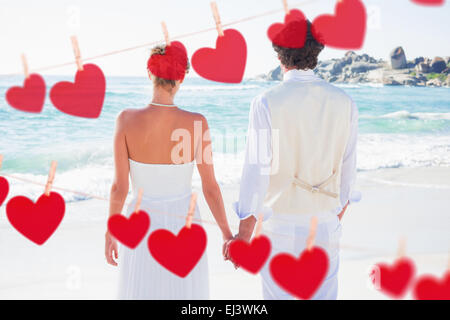 Composite image of bride and groom holding hands looking out to sea Stock Photo
