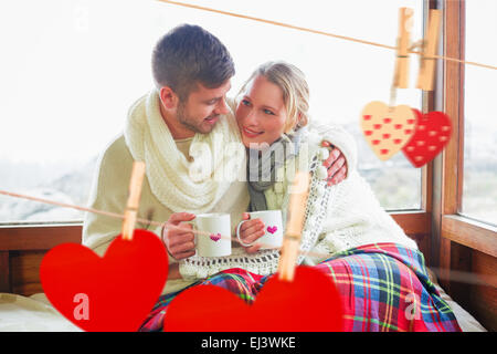 Composite image of loving couple in winter wear with cups against window Stock Photo