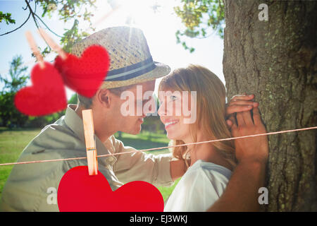 Composite image of cute smiling couple leaning against tree in the park Stock Photo