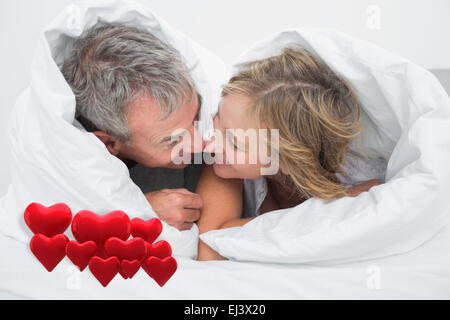 Composite image of loving middle aged couple under the duvet Stock Photo